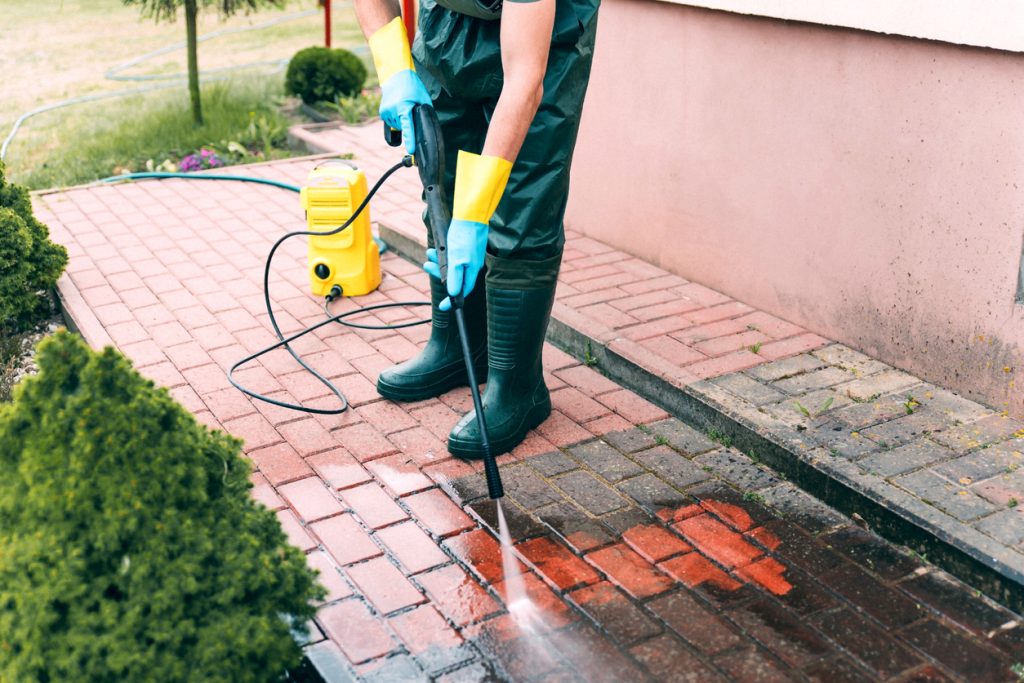 Man cleaning red, conrete pavement block using high pressure water cleaner. Paving cleaning concept Nettoyage de pavé uni ou brique par Lavage Pression Net avant / après